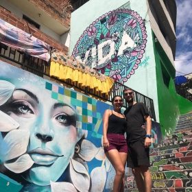Couple exploring Comuna 13 Medellín with colorful street art mural in the background.
